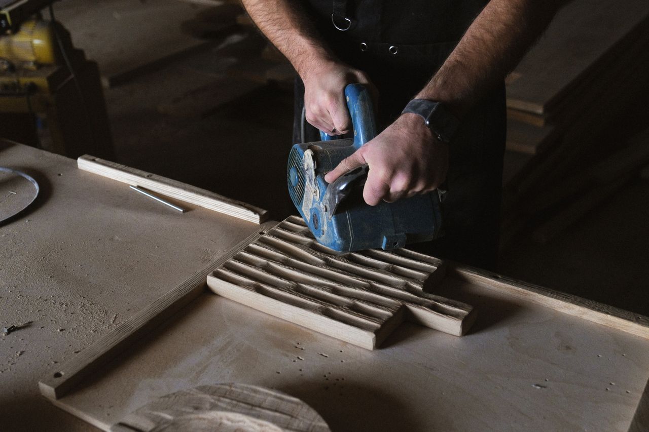 heros-img From above of anonymous craftsman using special electric tool to polish wooden board while working at table in professional joinery